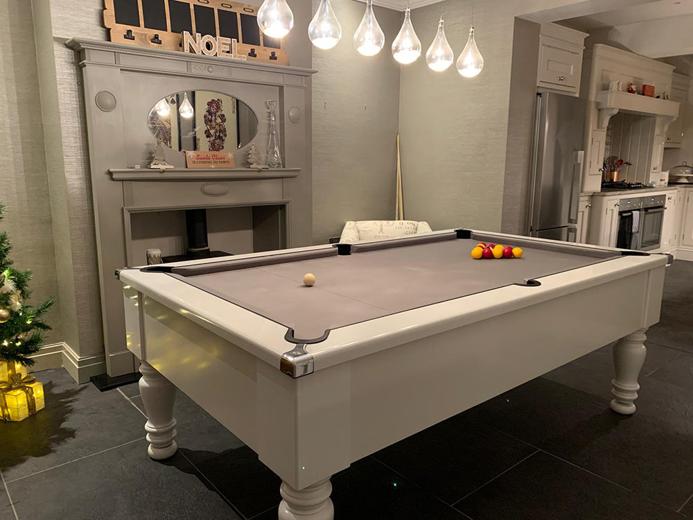 Gloss White Turned Leg Pool Table with grey cloth and chrome corners image on dark marble tiles.